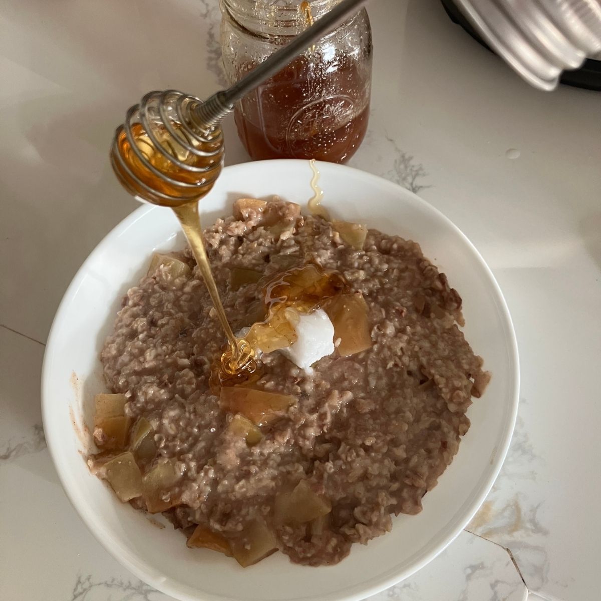A bowel of porridge with a honey spoon pouring honey over it.
